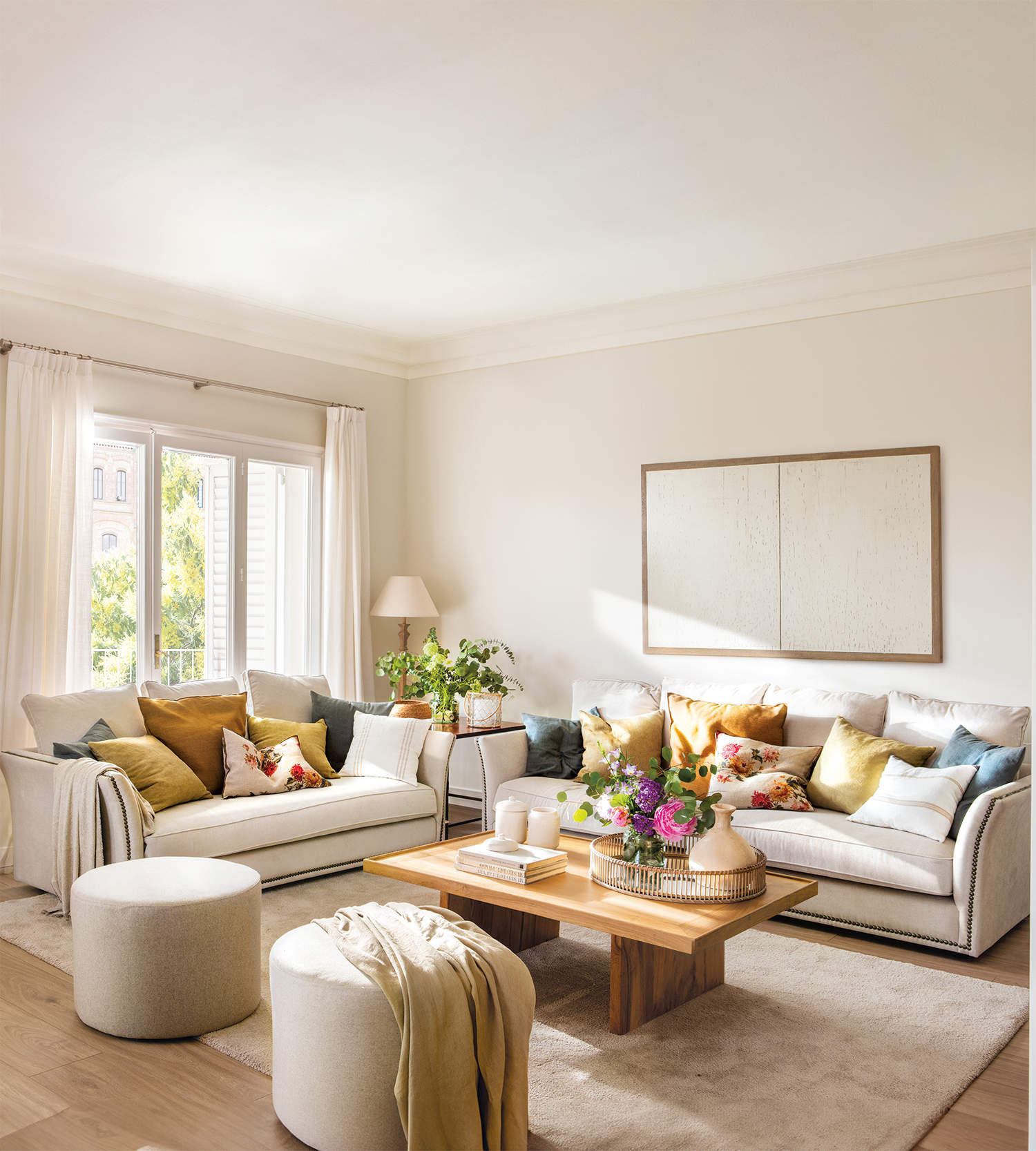 Salón cálido y luminoso con sofás beige y cojines azules, mostaza y floreados
